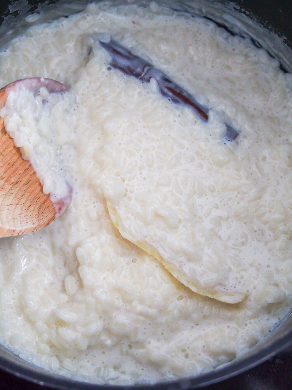 cooking arroz con leche (Spanish rice pudding) with a strip of lemon peel and cinnamon stick in pan