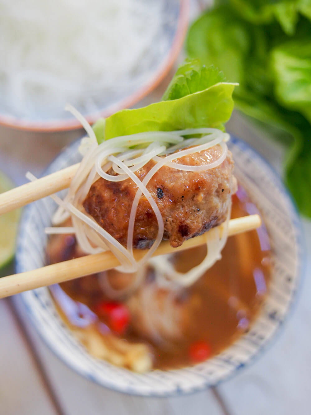chopsticks holding meatballs, noodles and some salad over dipping sauce
