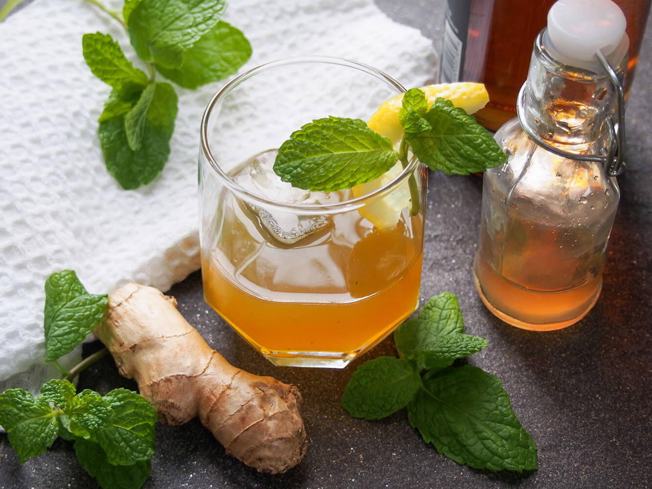 ginger whiskey smash with ginger syrup and whiskey bottles to side