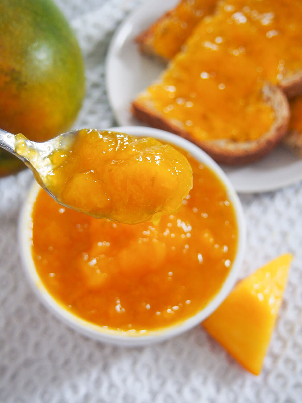 spoon with jam on it held above bowl with toast and mango behind