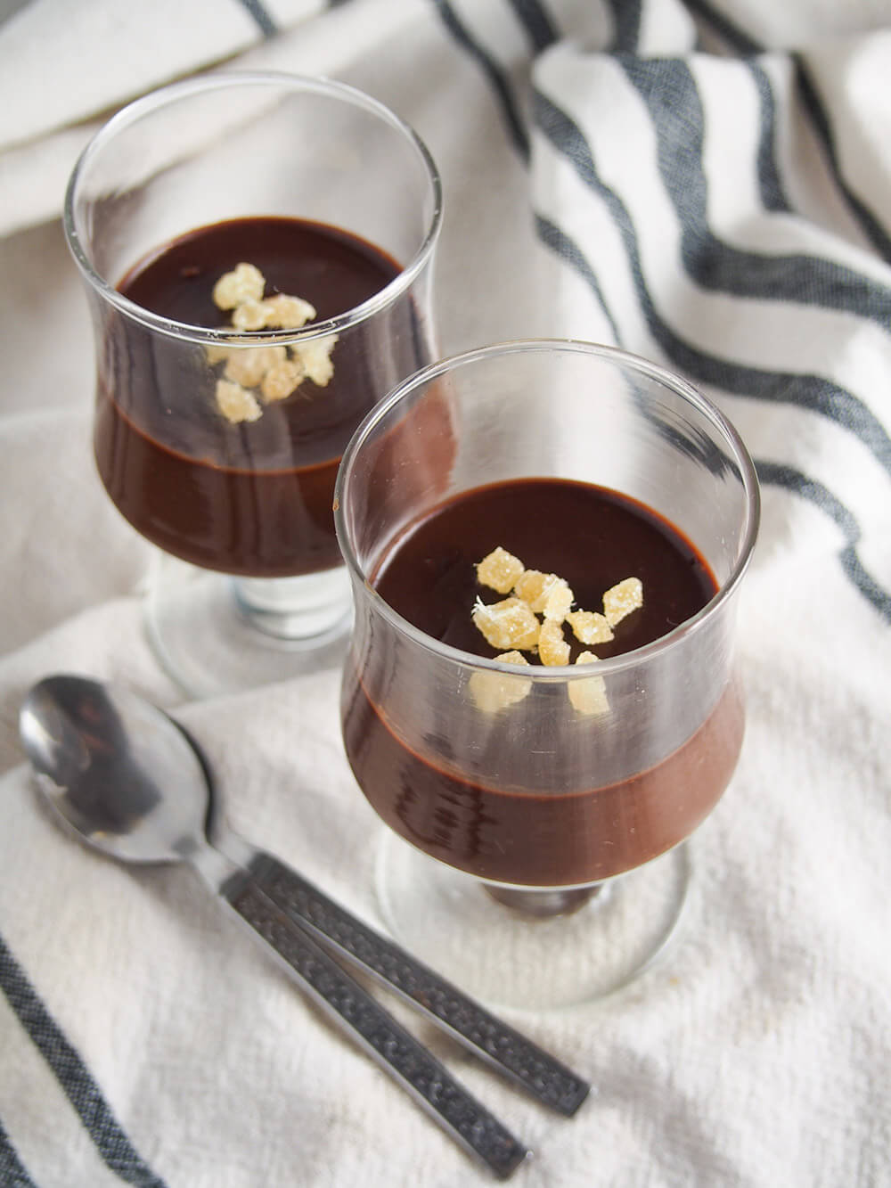 two glasses of no bake chocolate custard with crystalized ginger on top with spoons to side