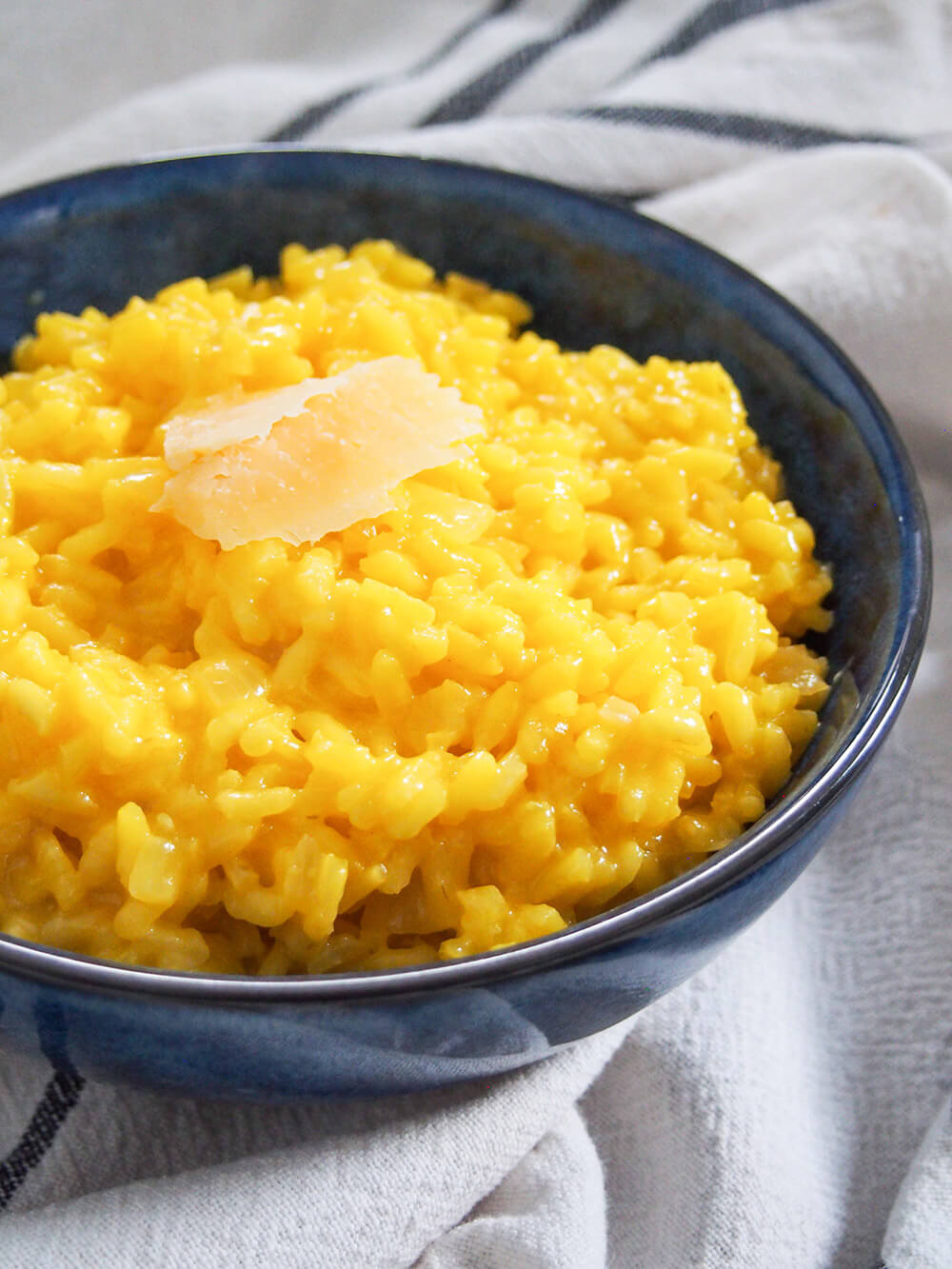 bowl of saffron risotto from side topped with parmesan shavings