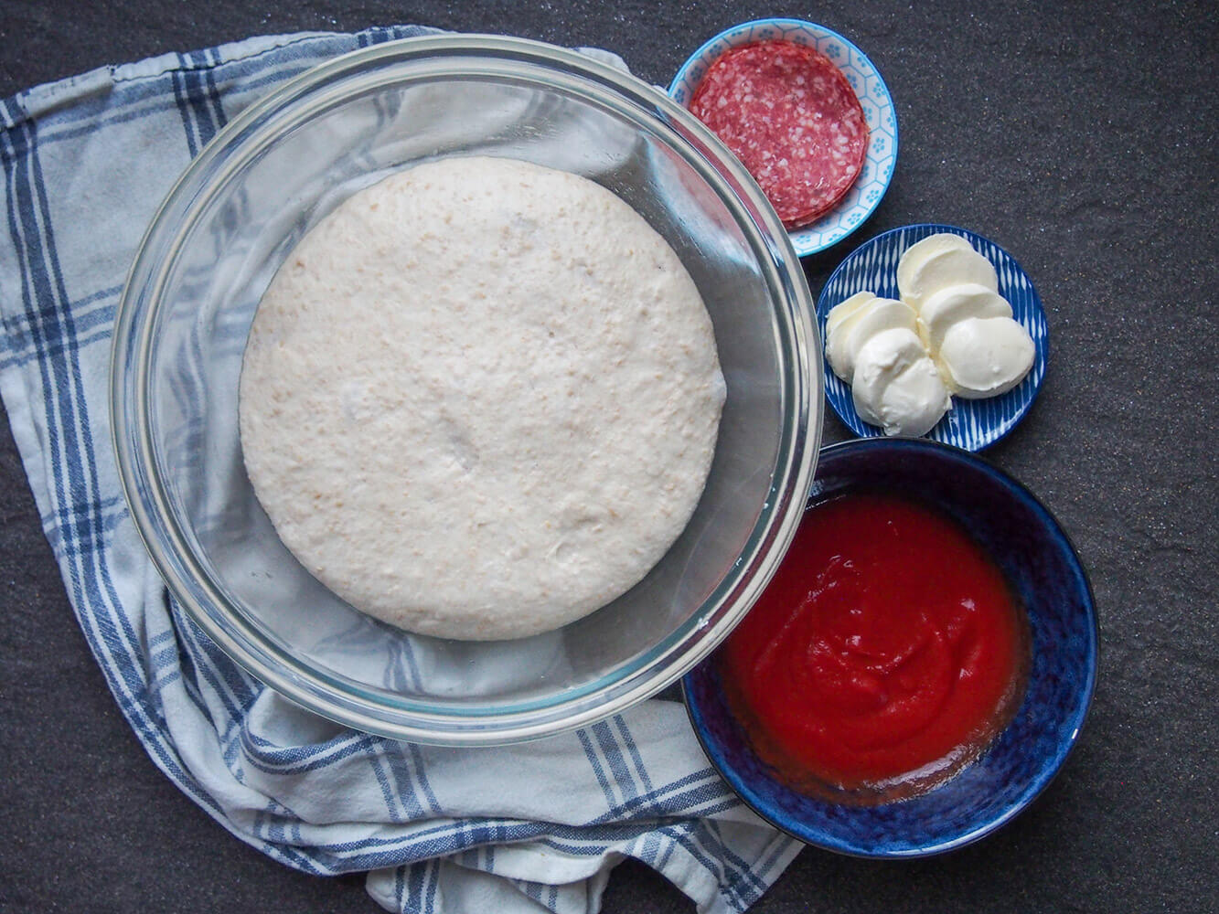 bowl of sourdough pizza dough with toppings to side