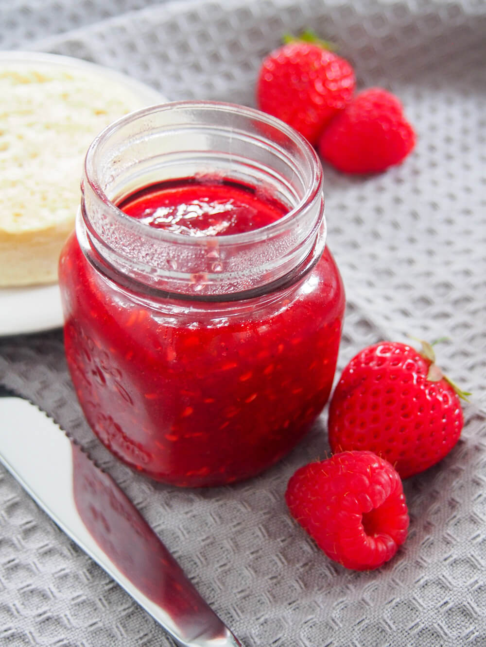 jar of strawberry raspberry jam with knife to one side and fruit to other