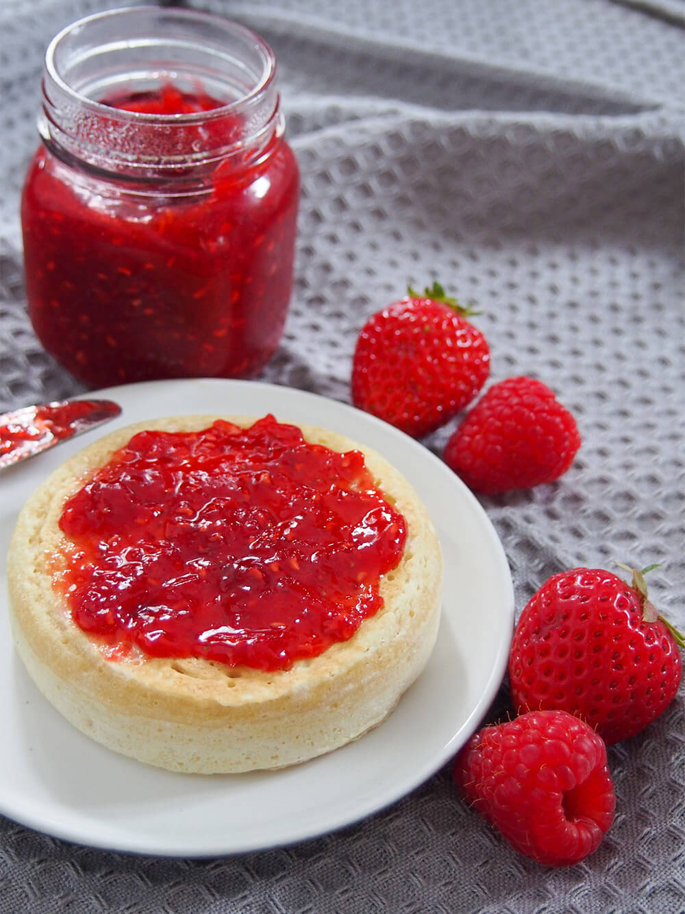 strawberry raspberry jam on crumpet with jar behind
