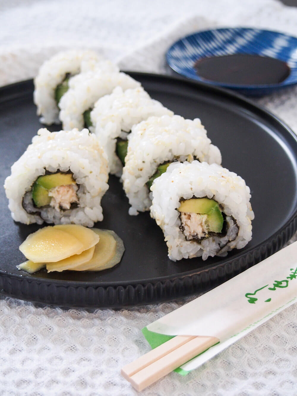 California roll in slices on plate with chopsticks in front and soy for dipping behind