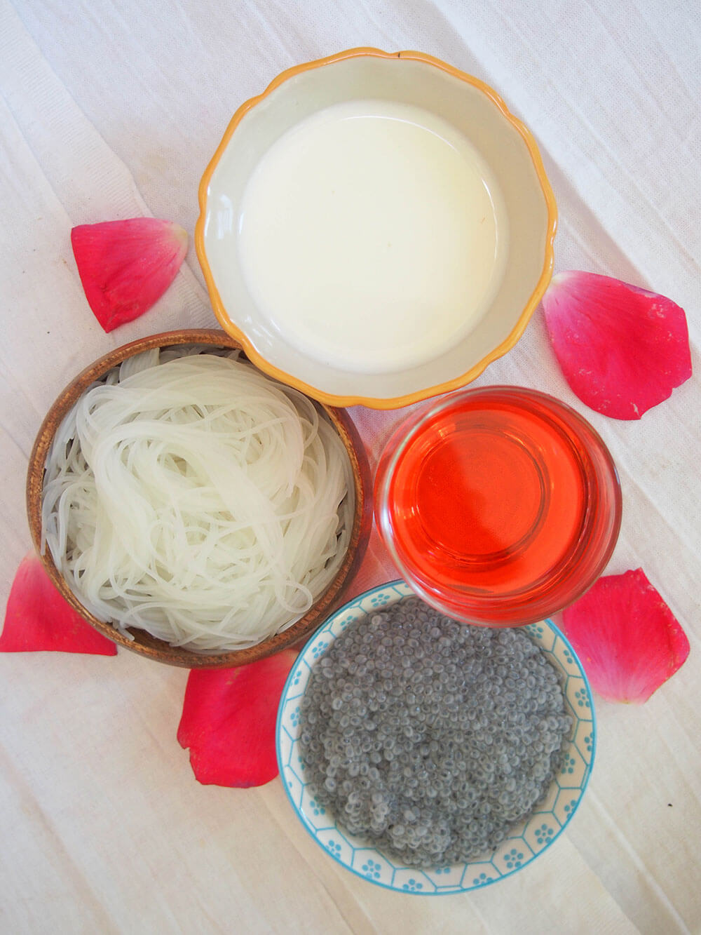 ingredients for falooda in separate bowls or dishes: vermicelli, soaked basil seeds, rose syrup and milk
