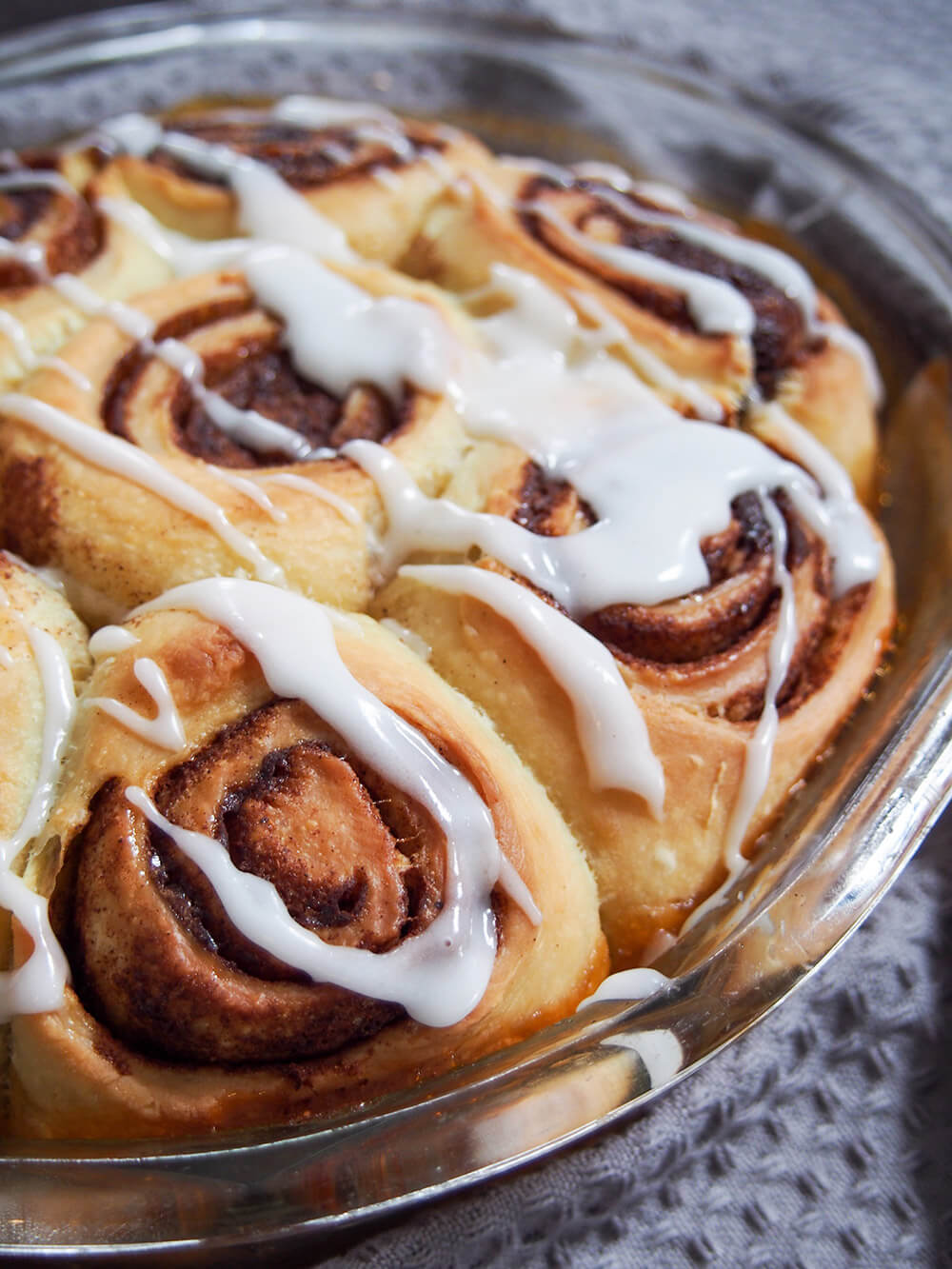 Give your starter a different use in these fluffy sourdough cinnamon rolls. They are packed with delicious flavor and have a wonderful texture. Prepare the night before or the same day as suits. glazed sourdough cinnamon rolls close up from side of dish