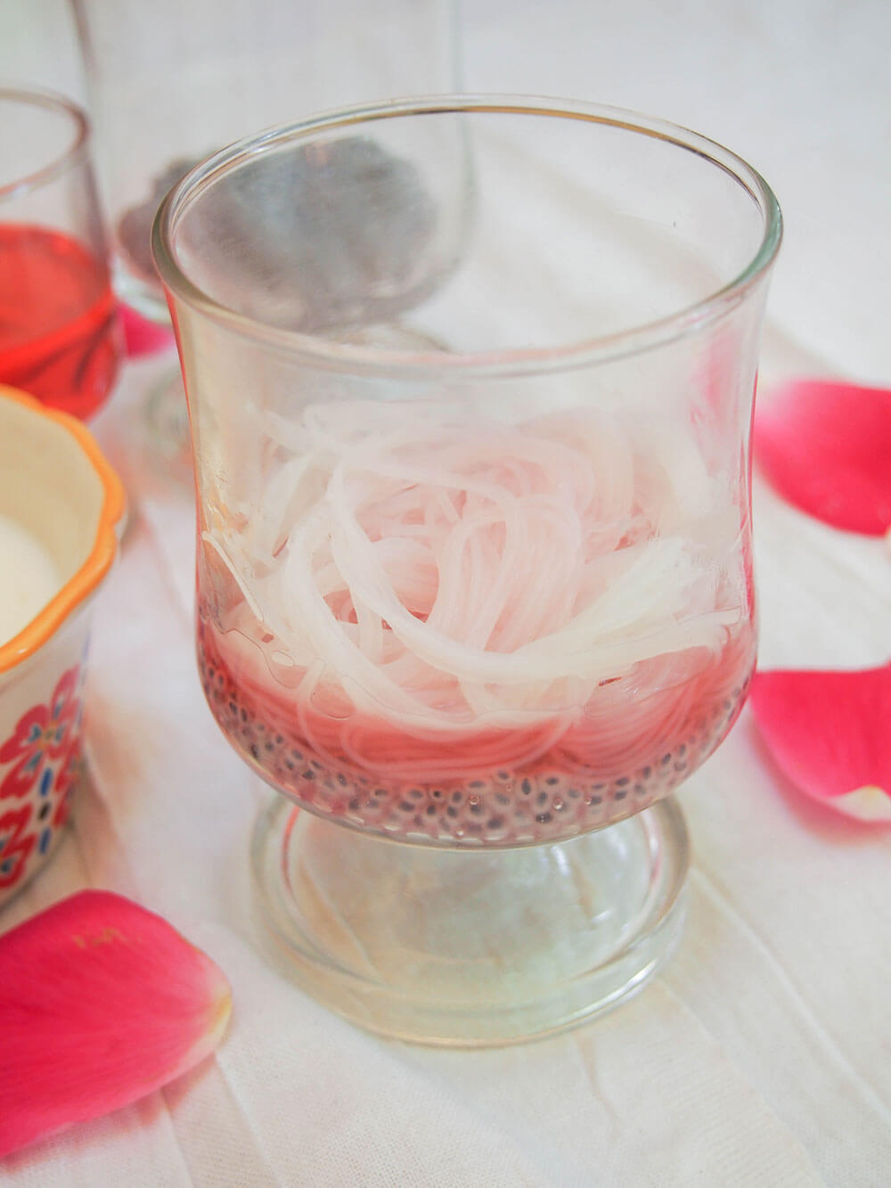 making falooda - layering basil seeds, vermicelli and rose syrup in glass before adding milk