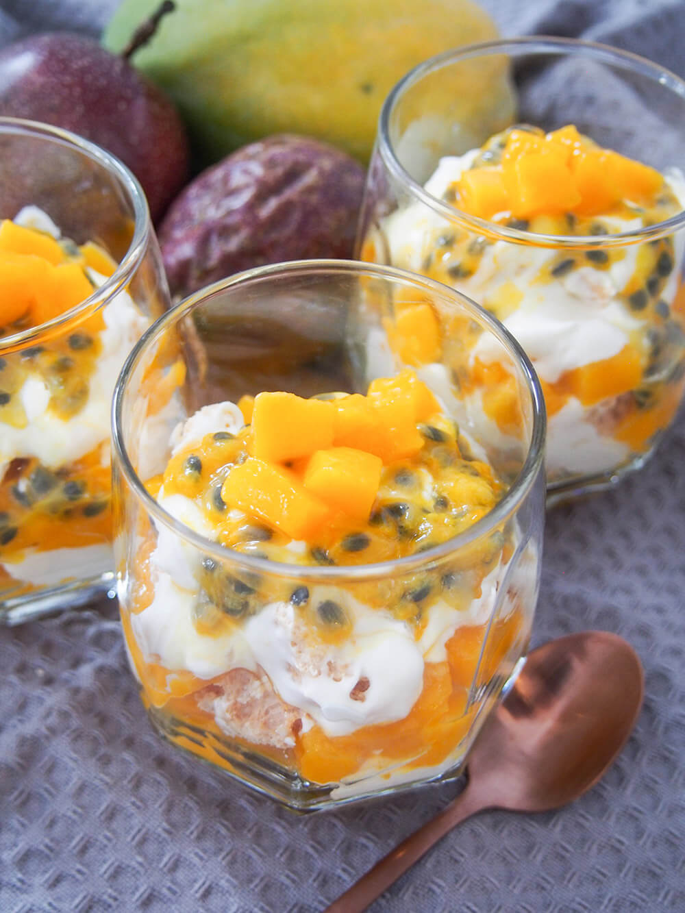 glass of Australian-style Eton mess showing mango and passion fruit on top, with other glasses and fruit behind