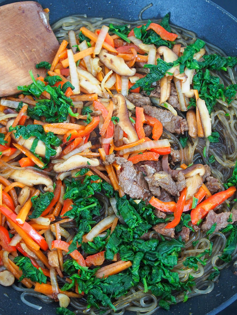 adding cooked beef and vegetables back in to noodles to finish up dish