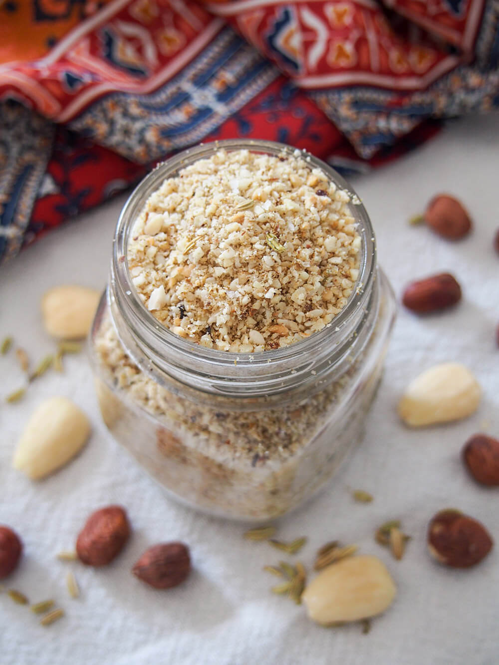 Dukkah is an Egyptian blend of nuts and spices that is easy to make and adds a wonderful crunch and flavor to so many things. Whether you dip bread in it, use it to top eggs or salads, it's a delicious addition. jar of dukkah with some of the nuts used in the mixture around jar