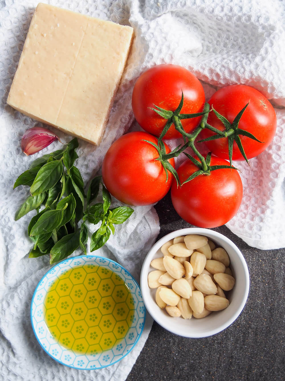 ingredients for sauce laid out - tomato, cheese, almonds, oil, basil and garlic