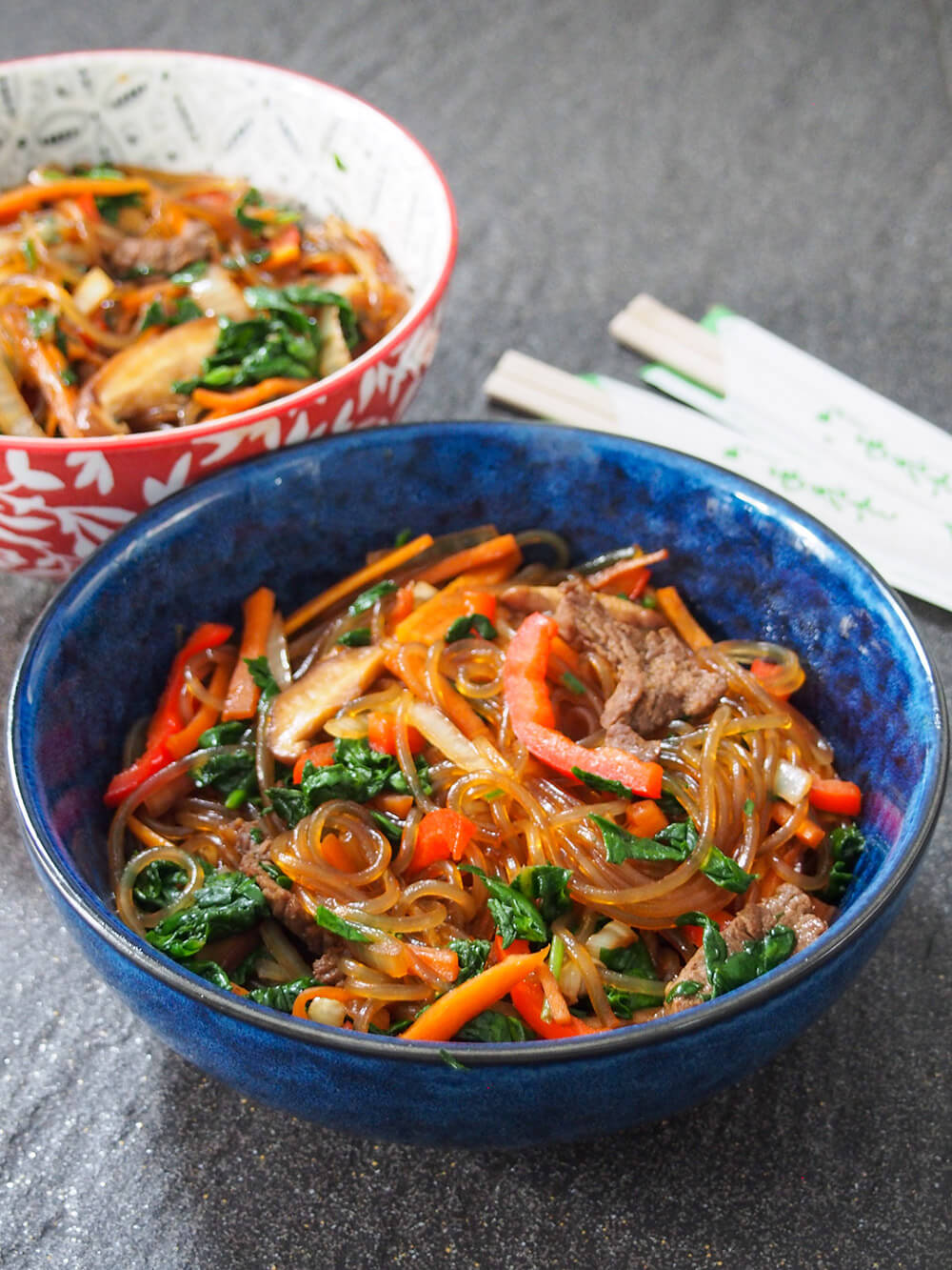bowl of japchae with second bowl and chopsticks behind