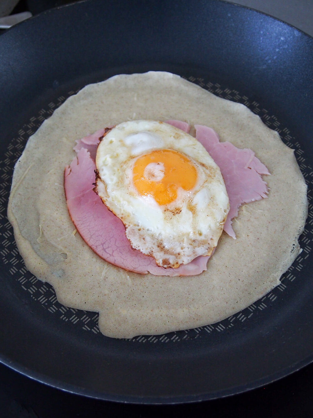 all toppings added to crepe - ham and egg visible over cheese