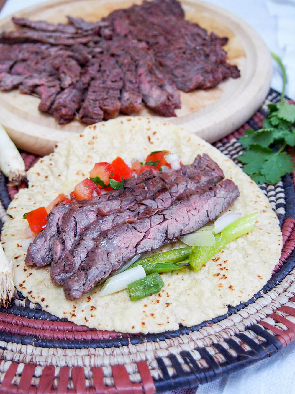 carne asada served in a taco with grilled green onions and pico de gallo