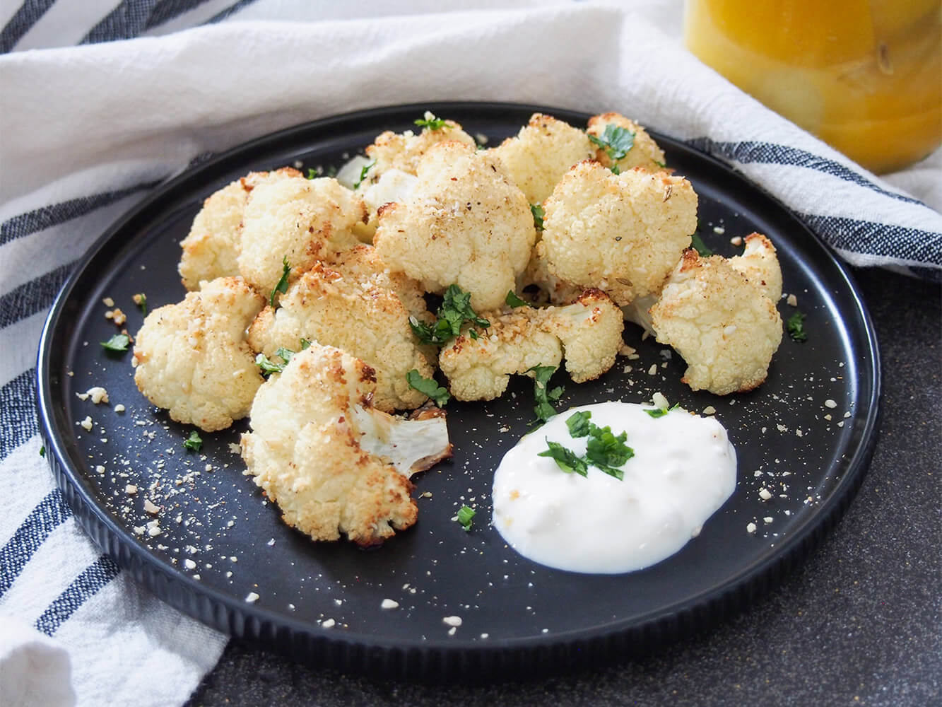 dukkah roasted cauliflower on plate with some preserved lemon yogurt in front