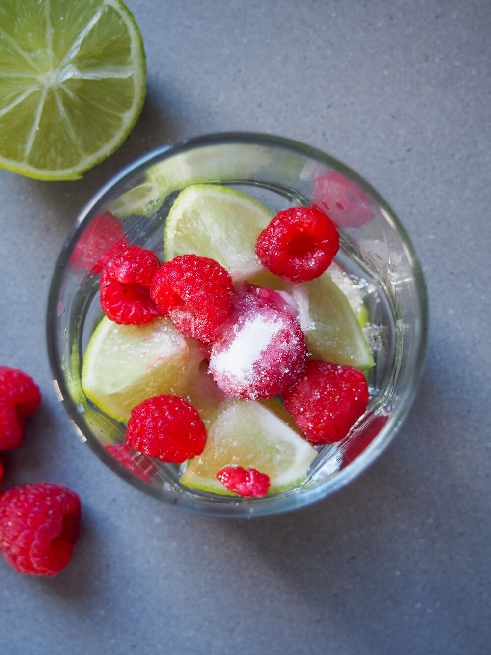 raspberries and lime in bottom of glass with some sugar on top