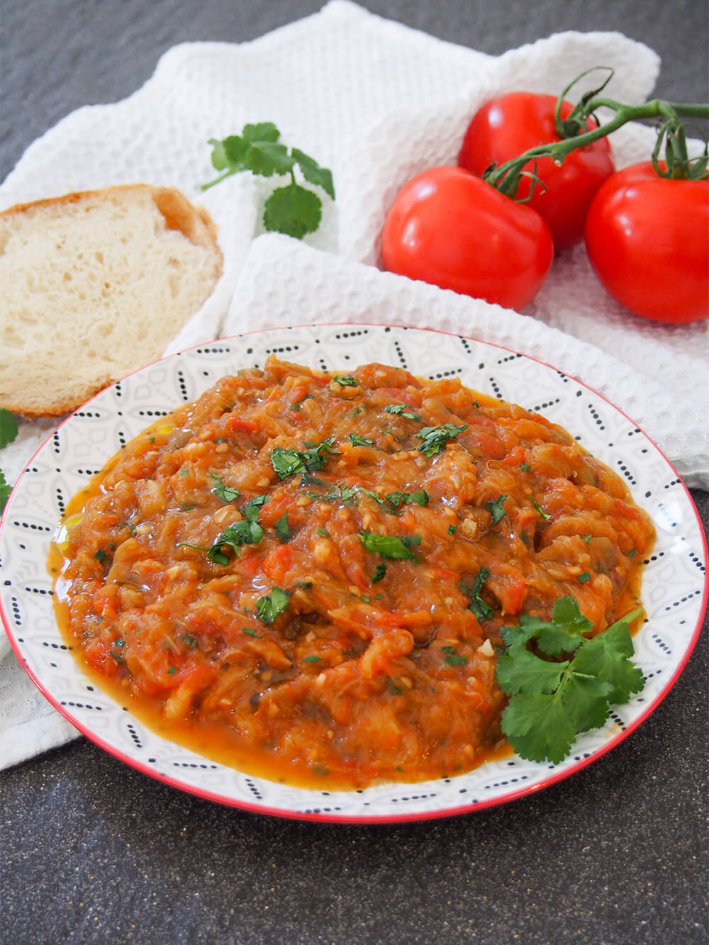 plate of Zaalouk (Moroccan eggplant salad) with bread and tomatoes behind