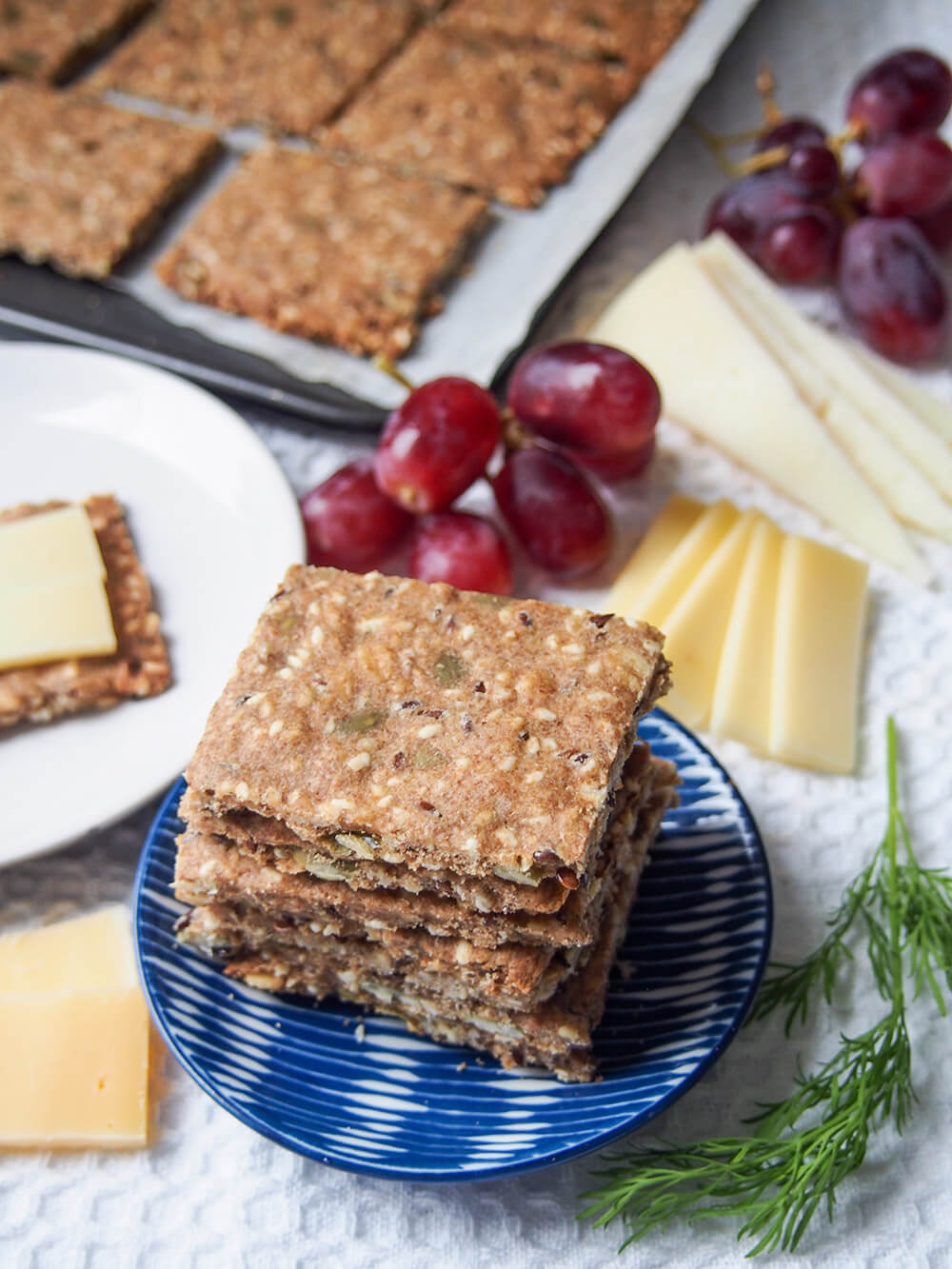 stack of Swedish crispbread (rye seed crackers) with more crackers, grapes and cheese behind