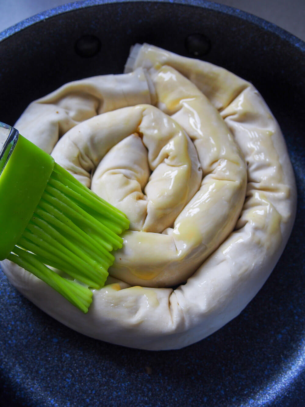 brushing pastry of coiled tikvenik with butter