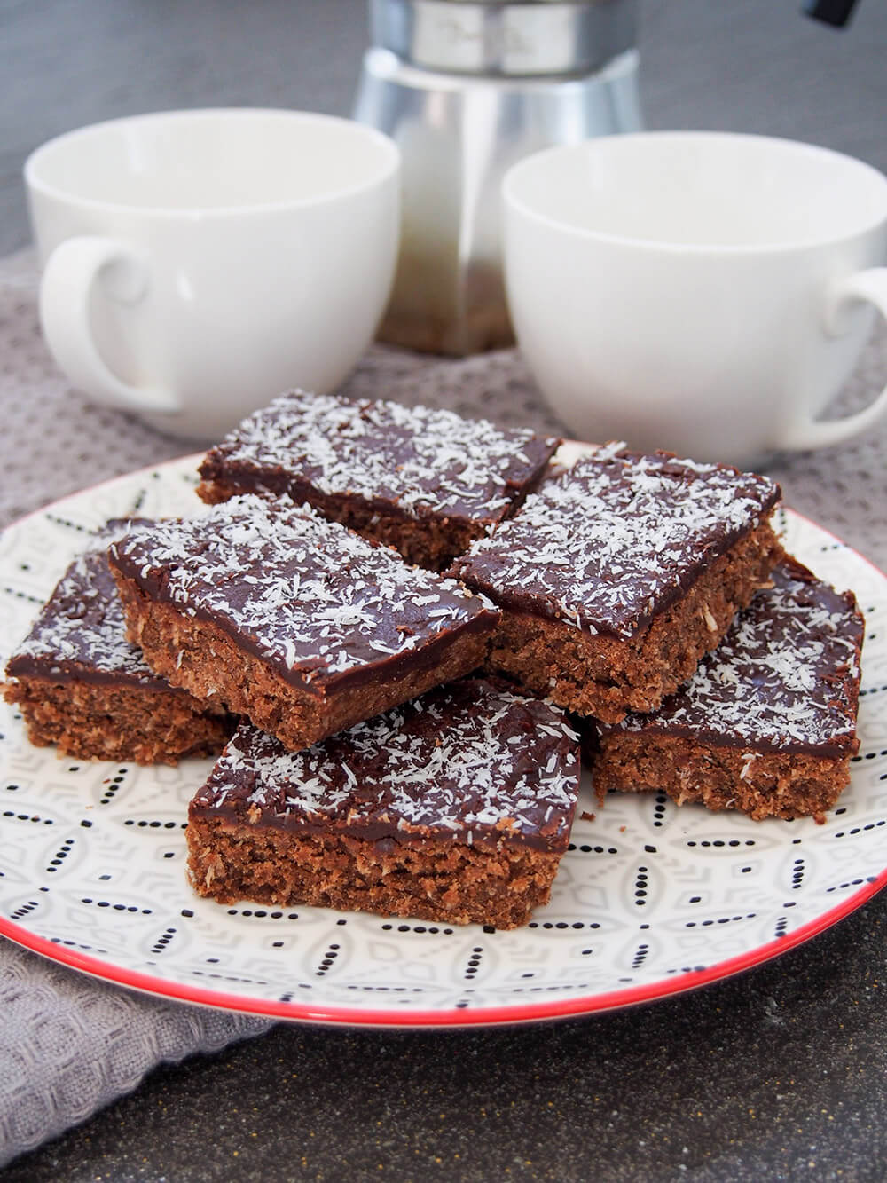 plate with slices of chocolate slice stacked with coffee cups behind