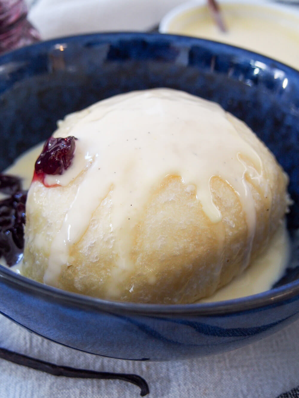 Dampfnudel is a steamed German sweet dumpling that's almost like a sweet bread, served with a luscious vanilla custard and often fruit compote. It's hearty but wonderfully comforting and delicious. close view of dampfnudel with vanilla sauce running down side