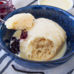 dampfnudel served with vanilla sauce over top and jam to side with spoonful resting on top