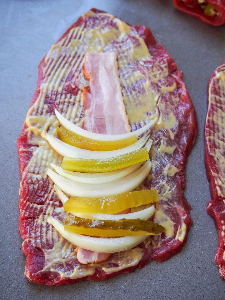 adding onion, pickle, bacon and mustard on top of beef