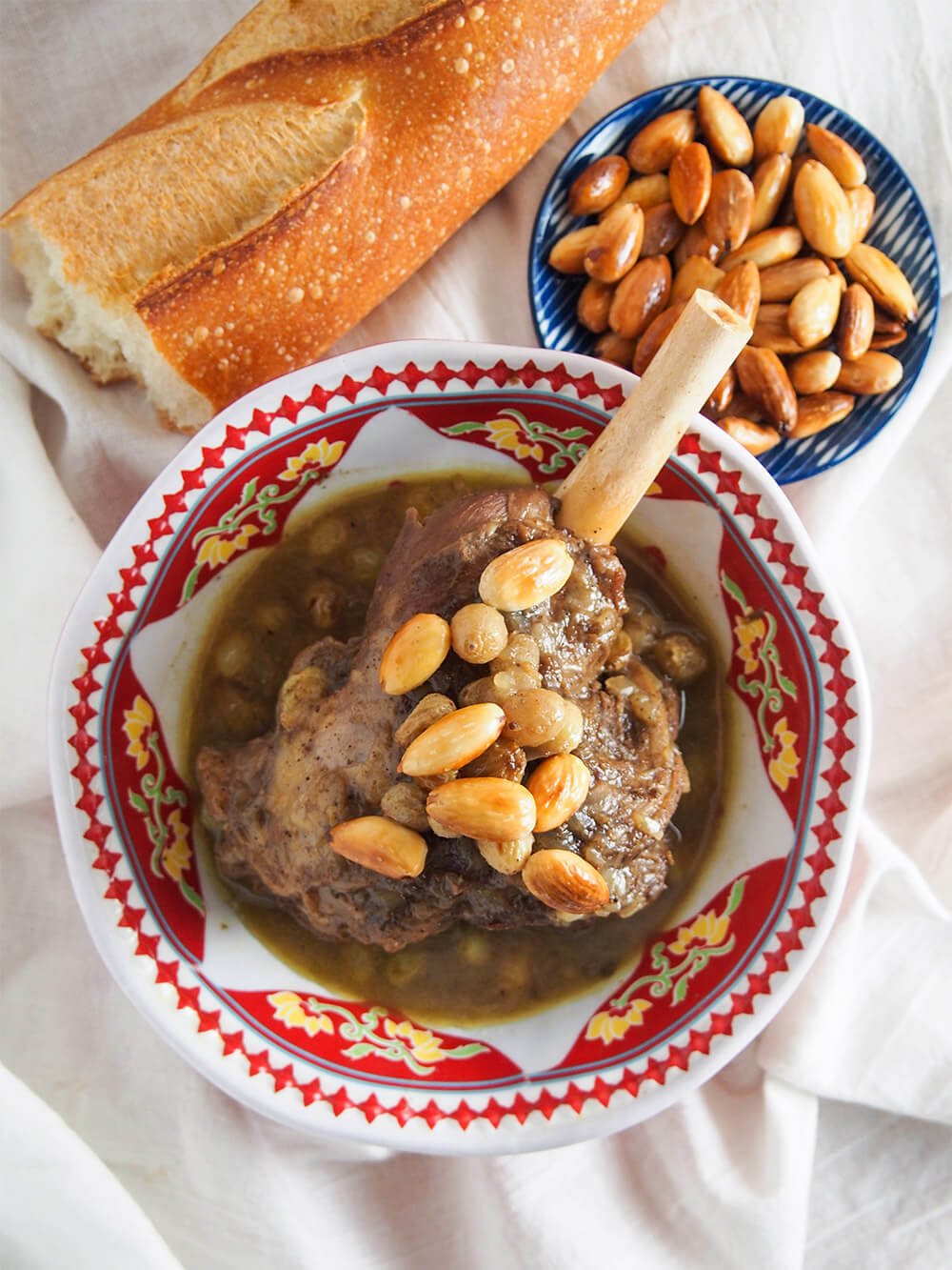 bowl of mrouzia honey lamb tagine from overhead with bread and plate of additional toasted almonds above