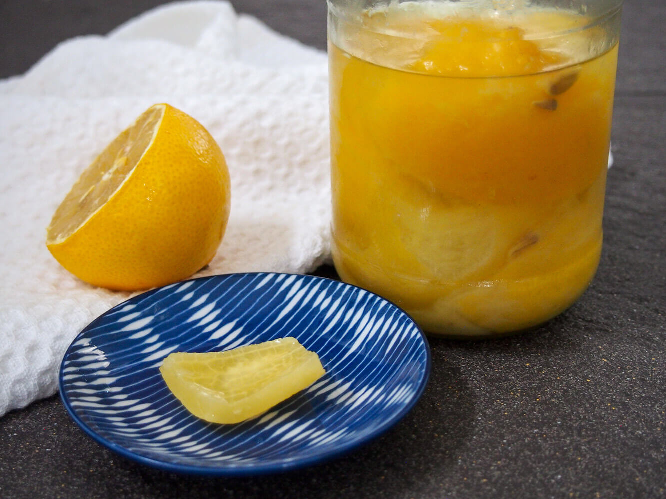 piece of preserved lemon in front of jar with more with fresh lemon half to side