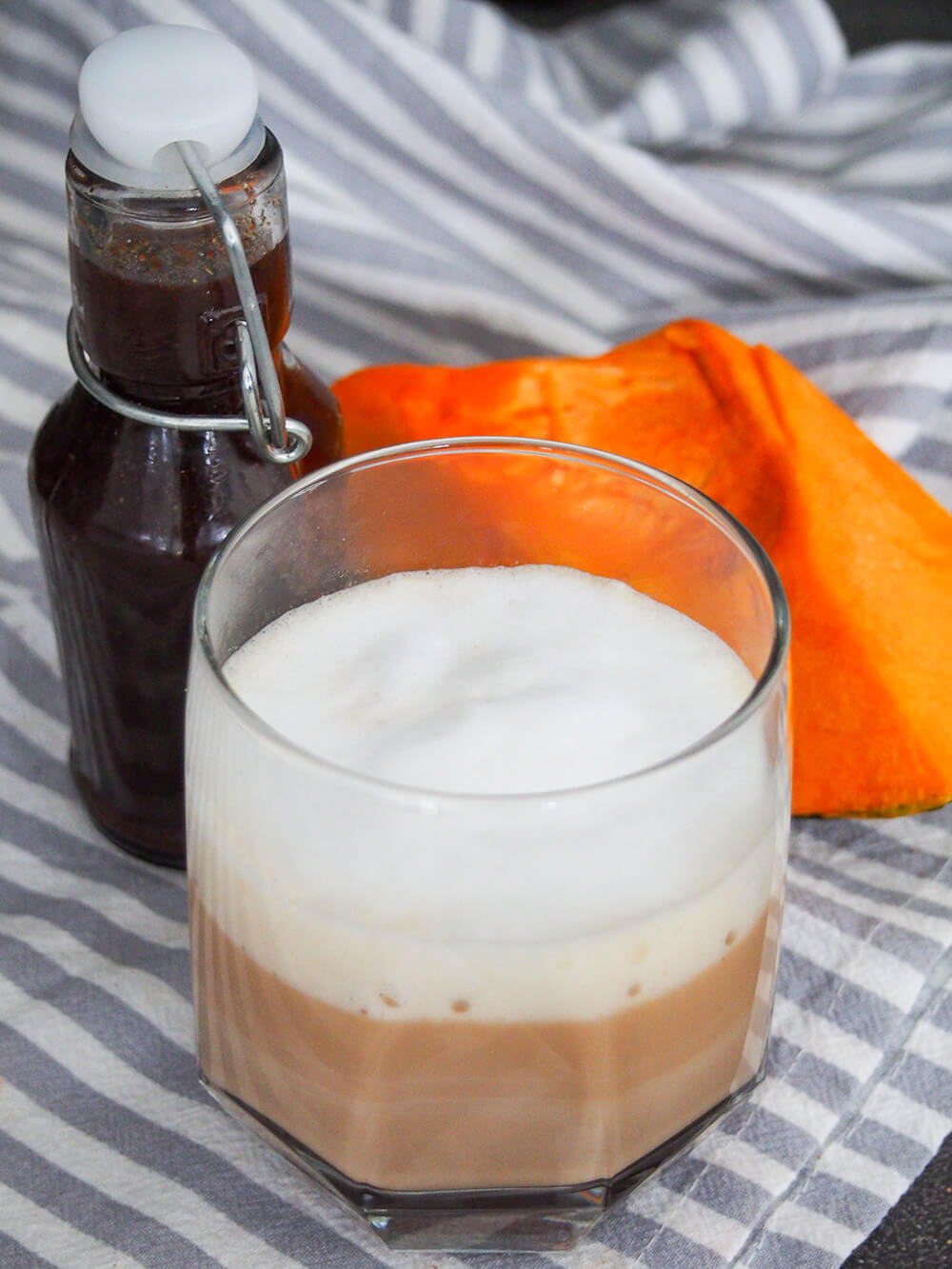 glass of pumpkin spice latte with bottle of syrup behind