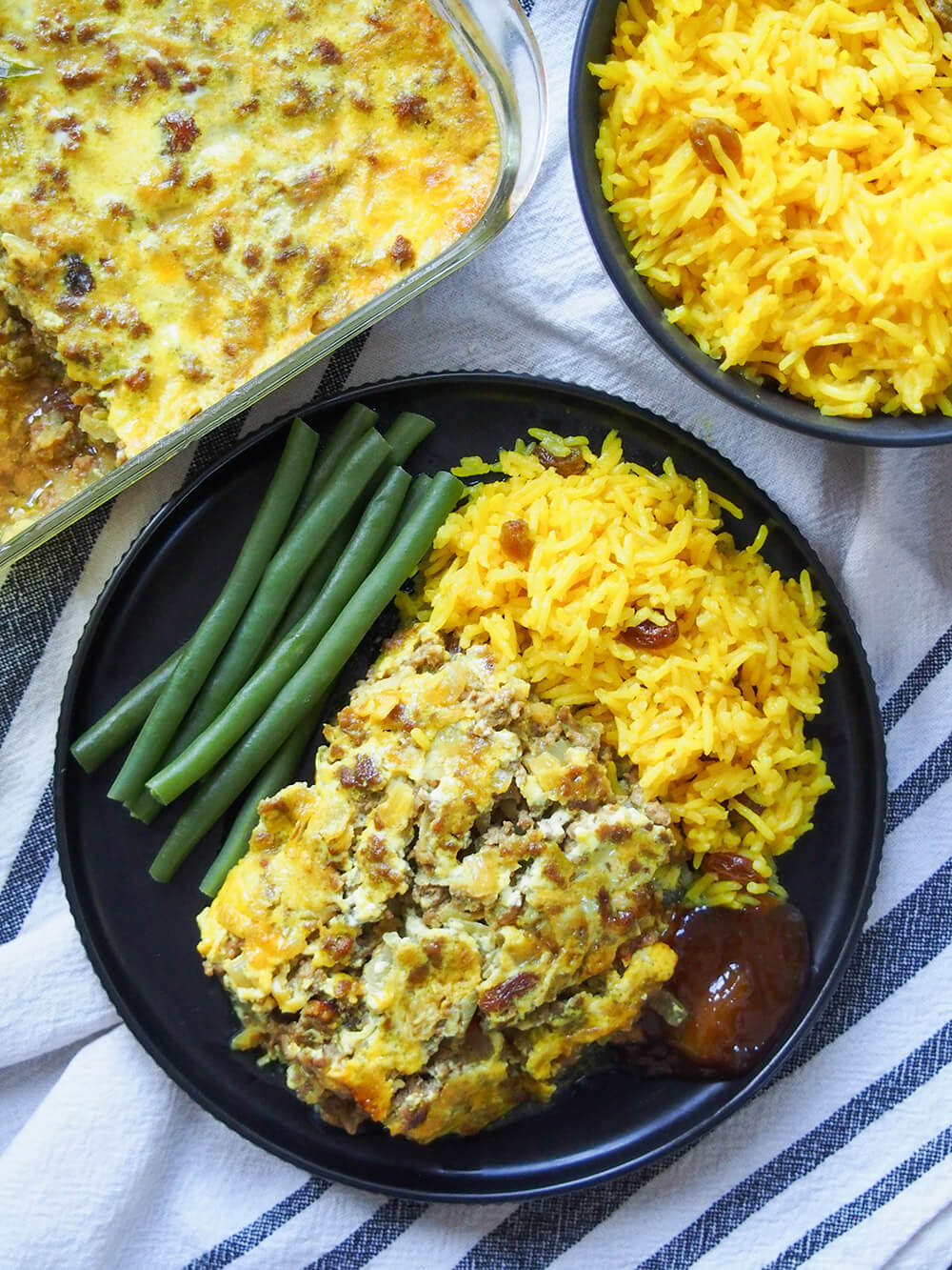 bobotie, rice and beans on plate from oerhead with more rice and bobotie dish above