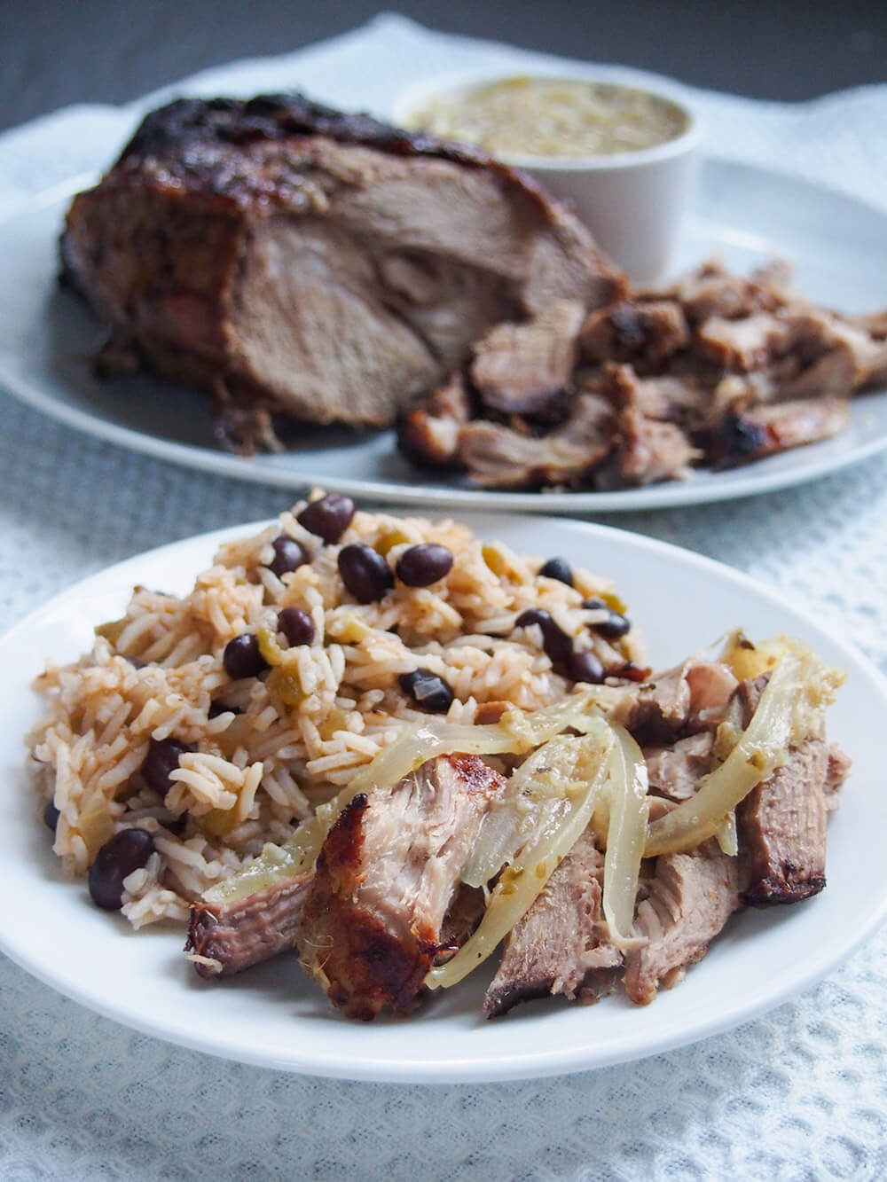 some of lechon asado on plate with rice and black beans and rest of pork behind