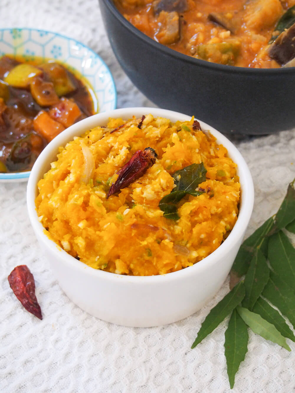 bowl of pumpkin erissery with bowl of sambar behind and pickle to other side
