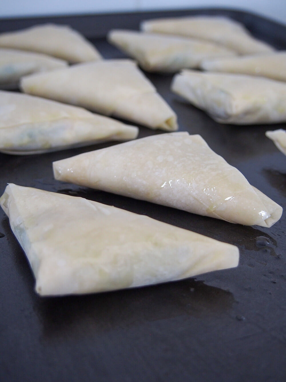 folded spanakopita on baking sheet ready to bake