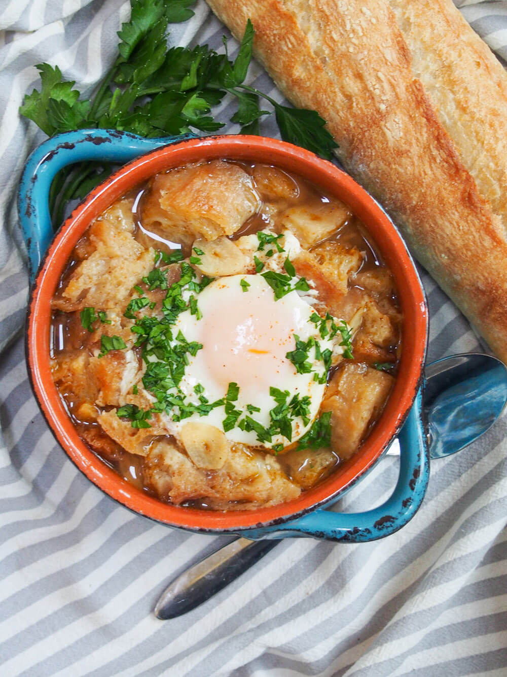 bowl of sopa de ajo from overhead with loaf or bread and spoon to side