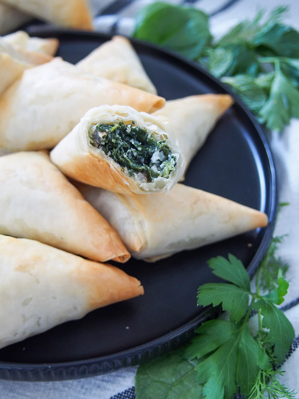 spanakopita triangles on plate with one bitten into resting on top