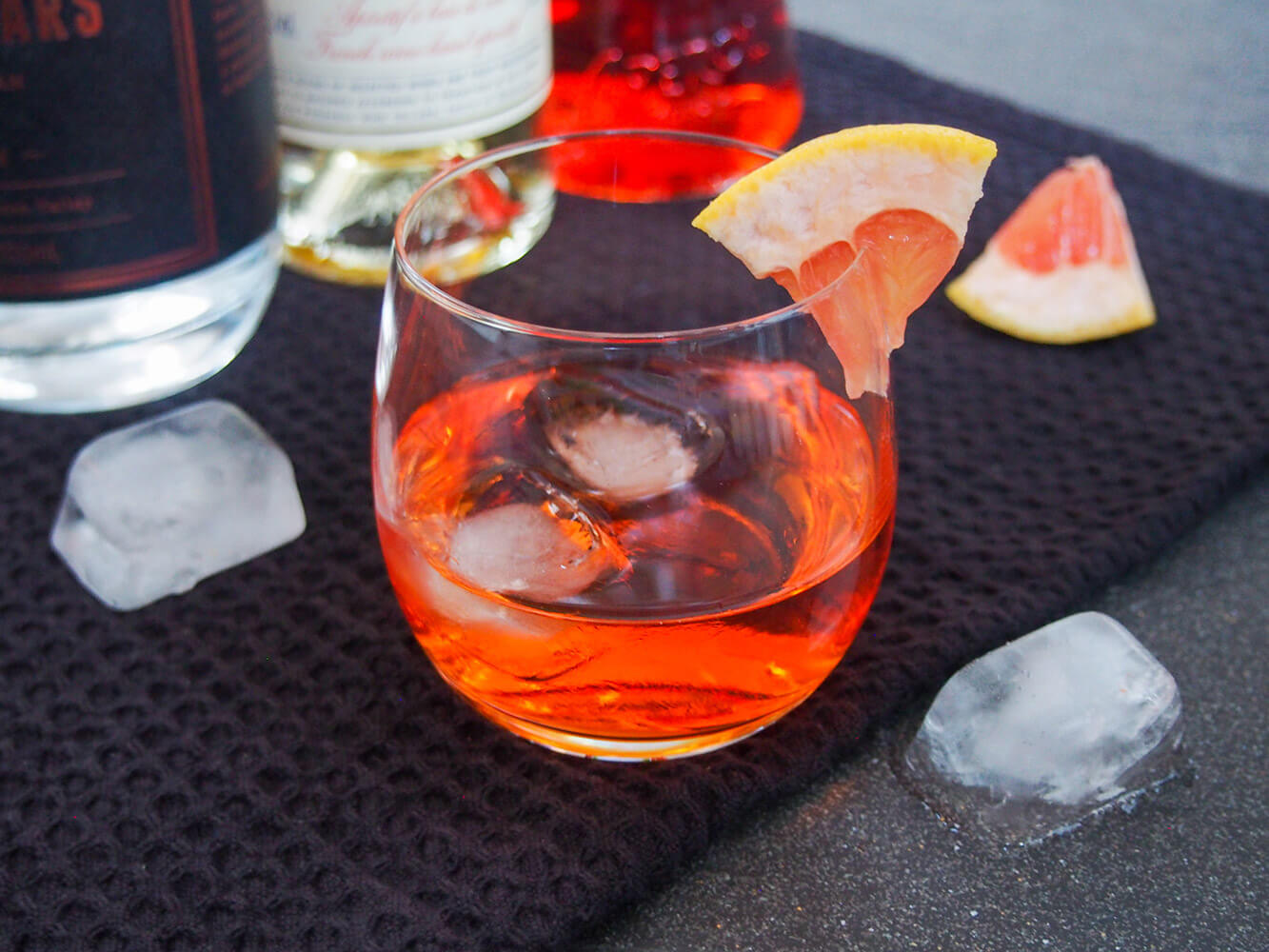 This unusual negroni has the same style of flavors as the classic, but is that bit more mellow and aromatic. Easy and wonderfully sippable. glass of unusual negroni with bottles behind