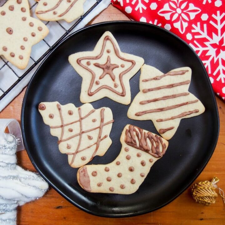 black plate with four German ginger cookies with others on rack to side, and some Christmas decorations on other sides