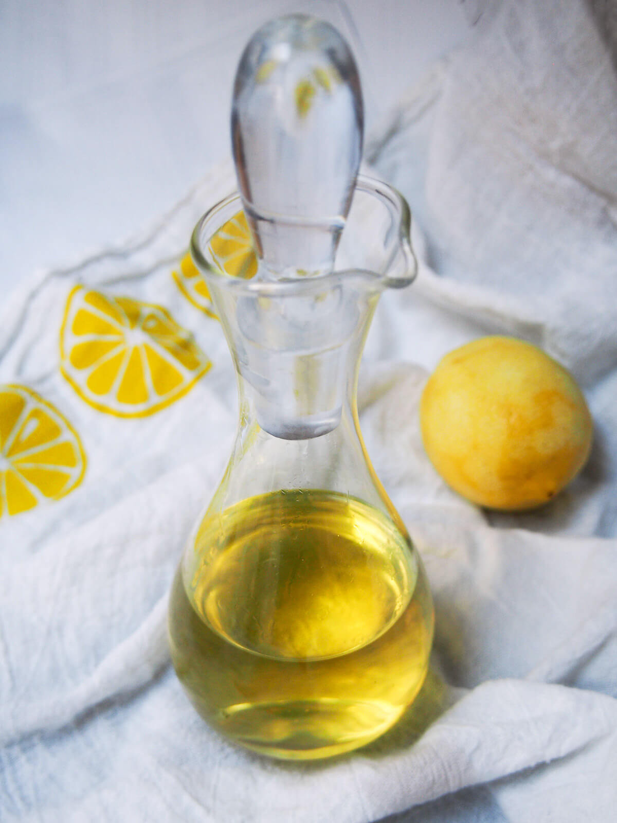 bottle of homemade limoncello with lemon to side on a lemon-print cloth