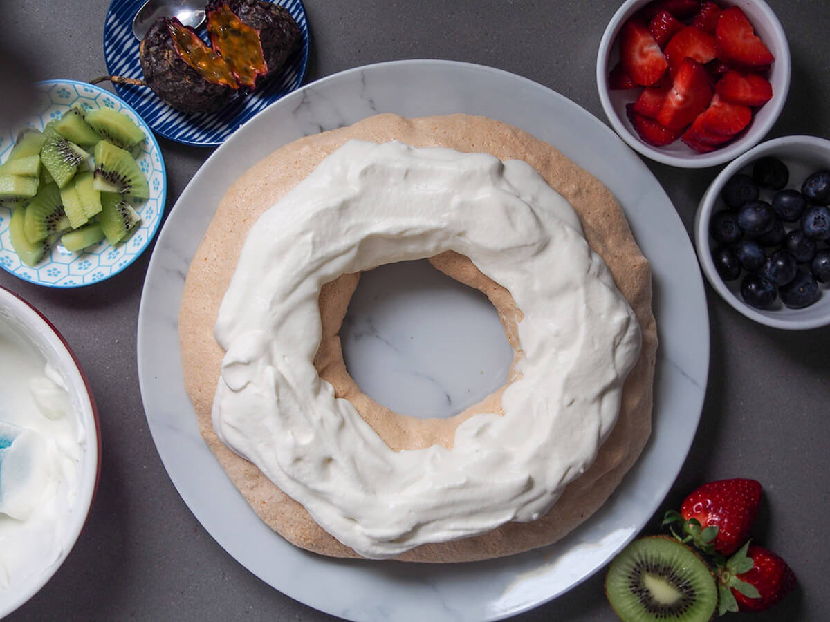 adding cream on top of meringue with fruit in bowls to side