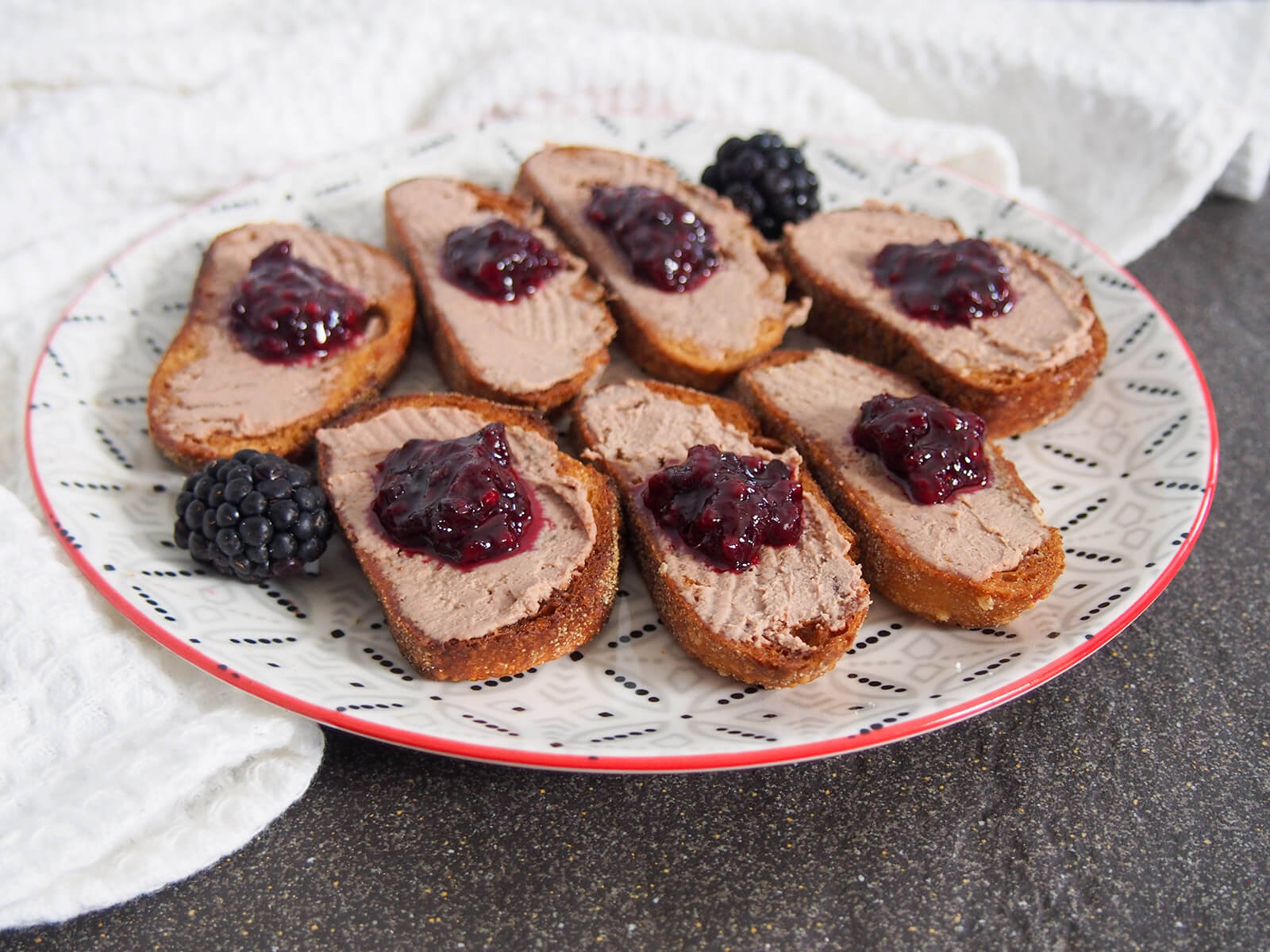 plate of chicken liver pate crostini topped with blackberry jam