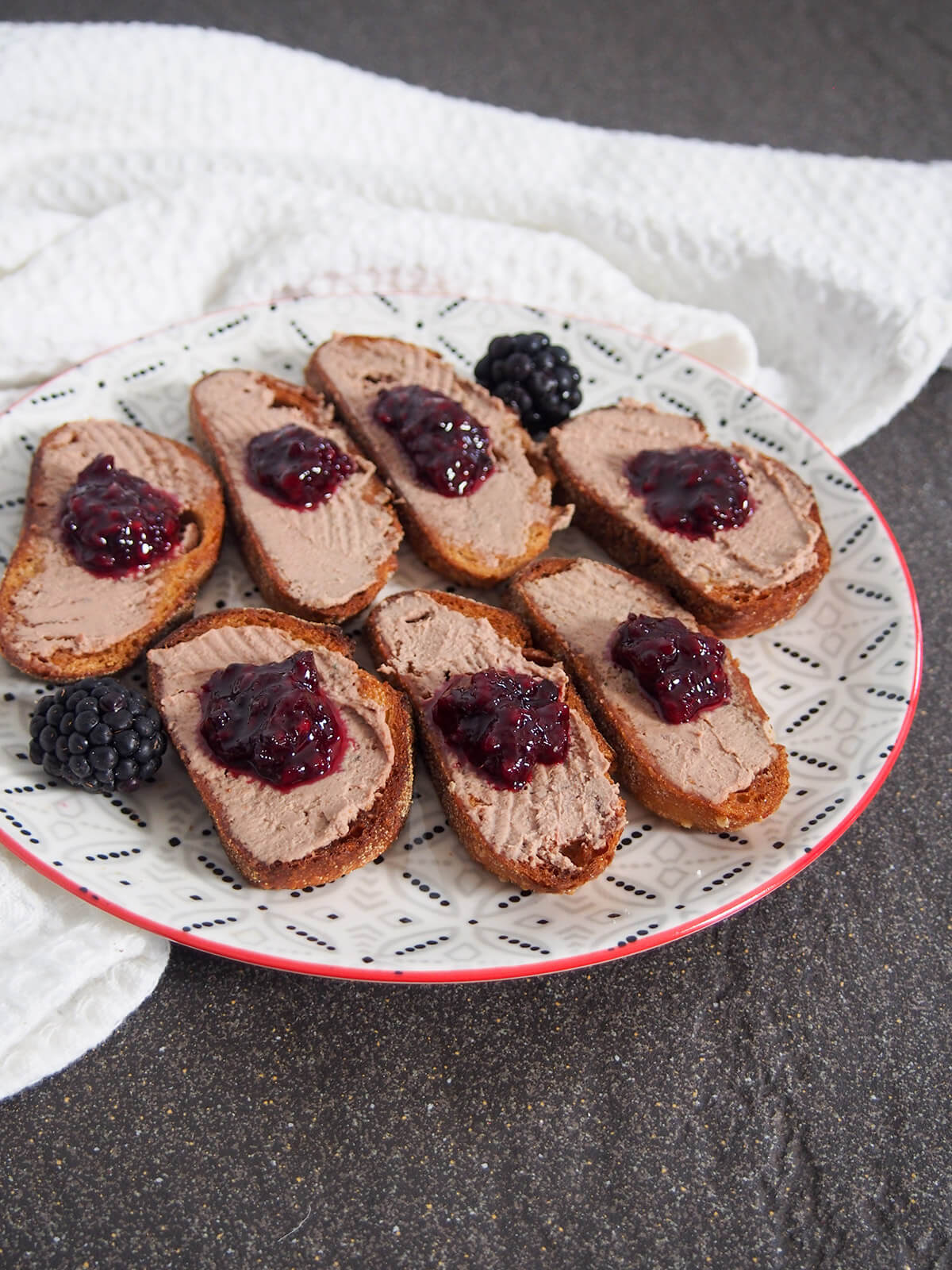 plate of chicken liver pate crostini with blackberry jam and blackberries to side of plate