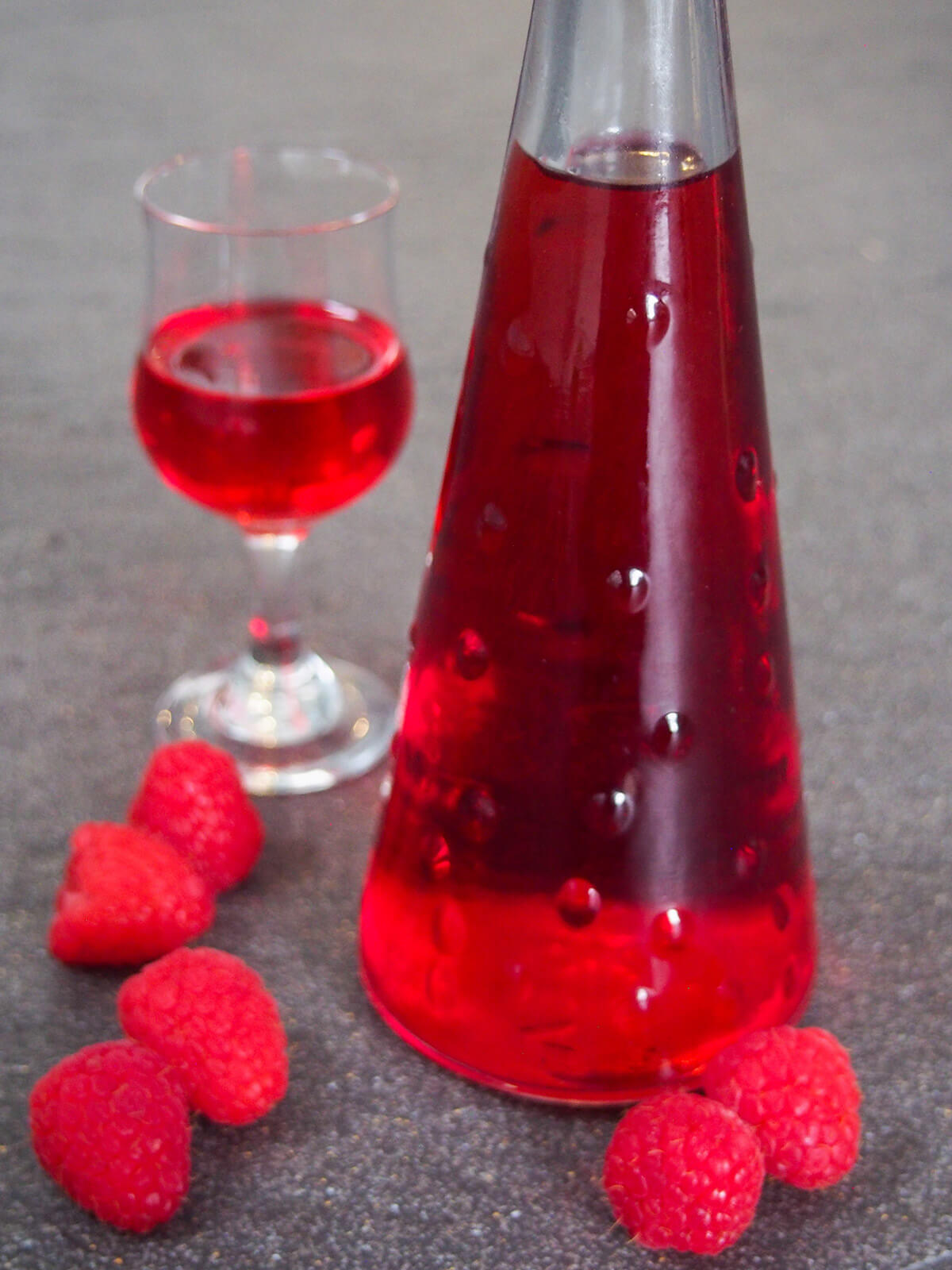 bottle of raspberry liqueur with raspberries to side and glass behind
