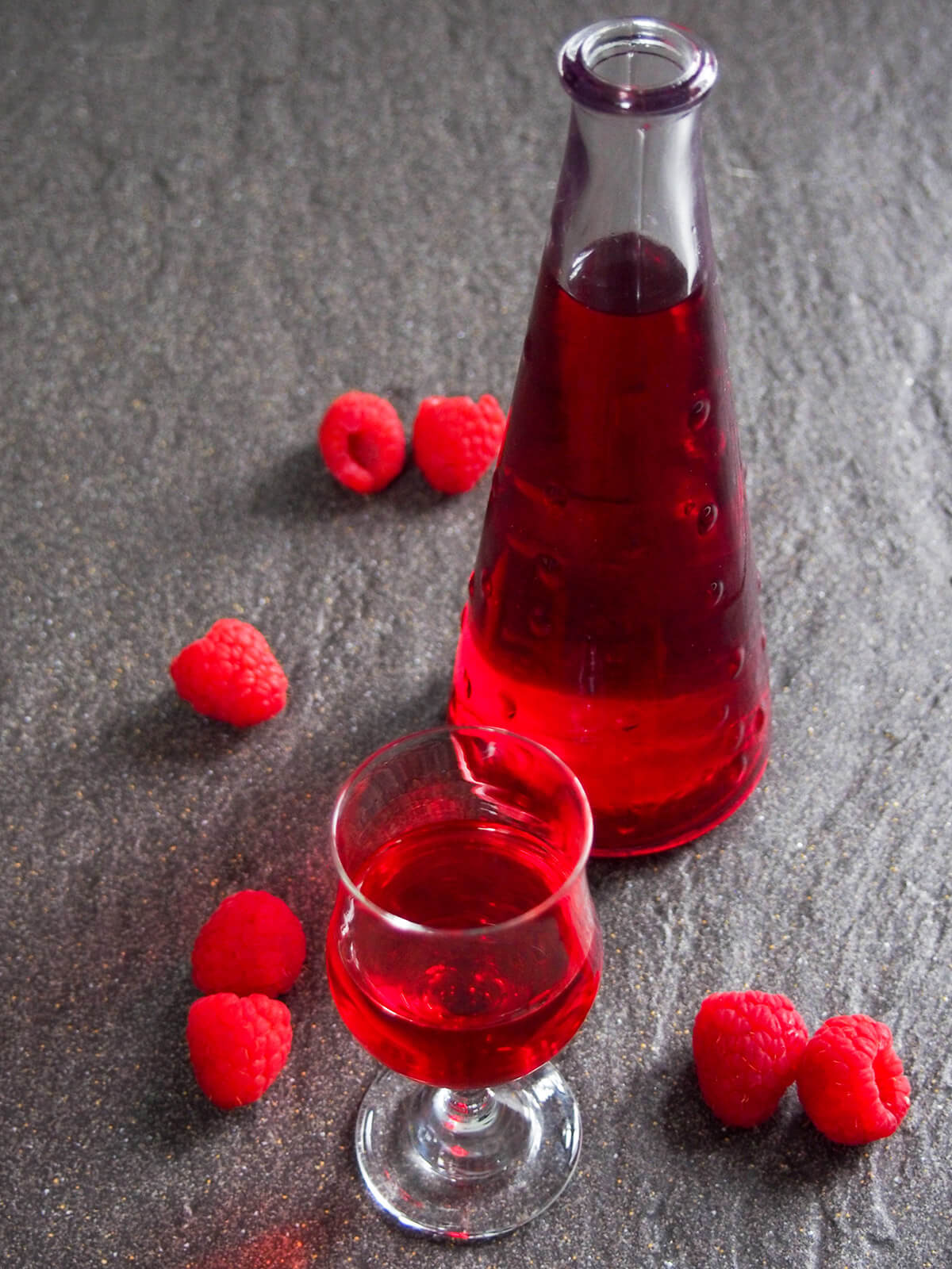 glass and bottle of raspberry liqueur with raspberries around