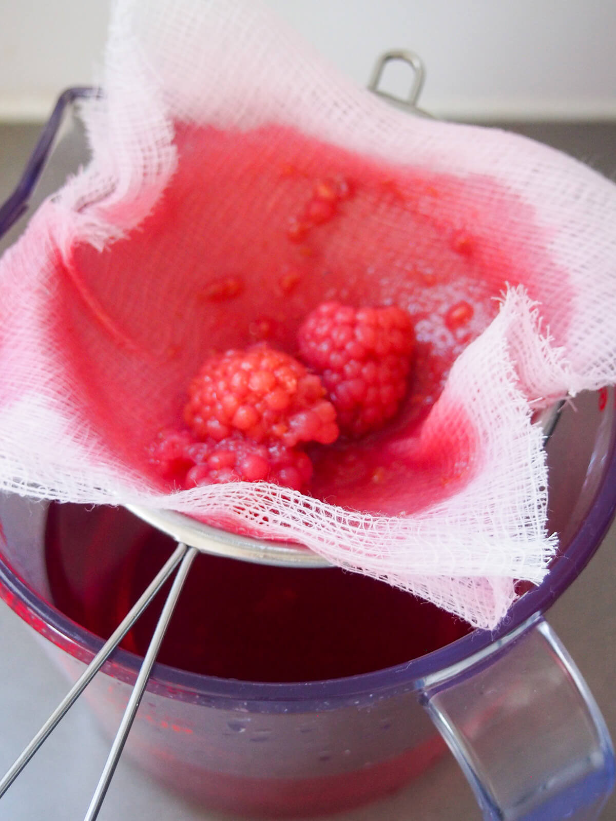 straining raspberry liqueur through cheesecloth lined strainer
