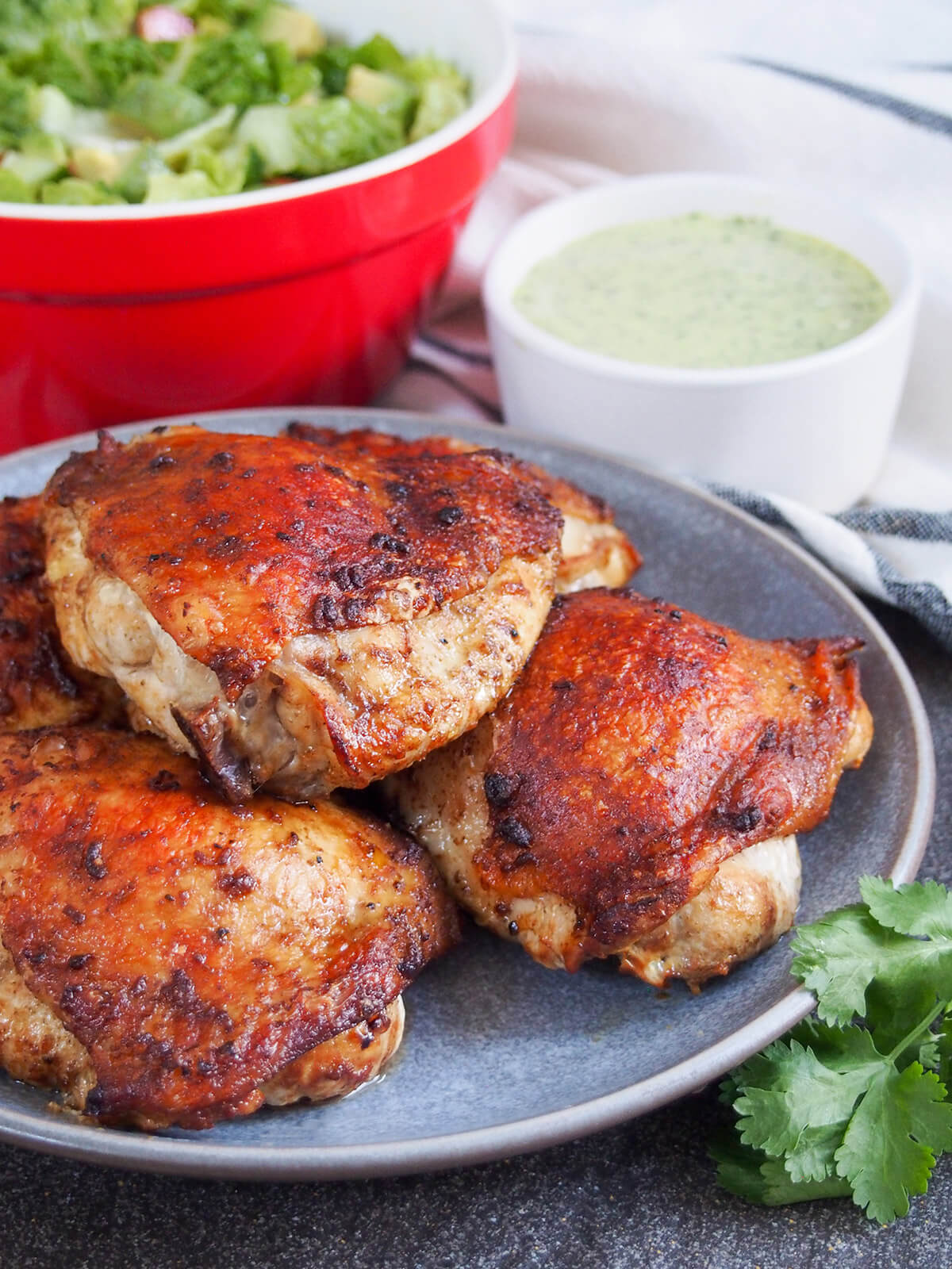 Peruvian roast chicken is traditionally made with whole chickens on a spit, but you can recreate the deliciousness with your oven. A simple but flavorful marinade adds an extra layer of flavor. plate of Peruvian roast chicken pollo a la brasa with aji verde sauce behind