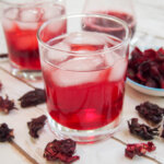 glass of hibiscus tea with ice in glass with hibiscus flowers to side