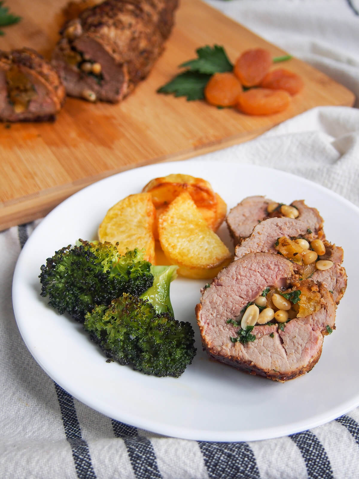 apricot stuffed pork tenderloin with broccoli and potatoes on plate with rest of stuffed pork behind